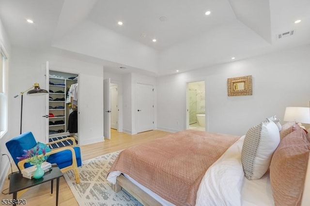 bedroom with a raised ceiling, light wood-style floors, a walk in closet, and recessed lighting