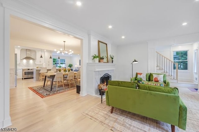 living area with stairway, light wood-type flooring, a chandelier, a warm lit fireplace, and recessed lighting