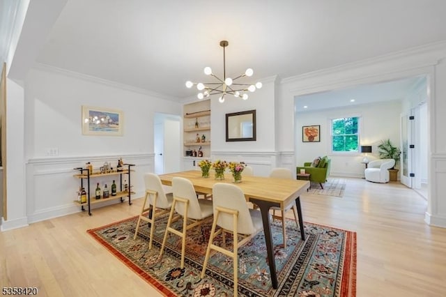 dining space featuring a chandelier, light wood finished floors, crown molding, a decorative wall, and built in shelves