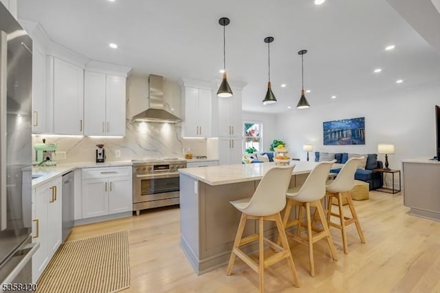 kitchen featuring wall chimney range hood, stainless steel appliances, open floor plan, light wood-style flooring, and a kitchen island