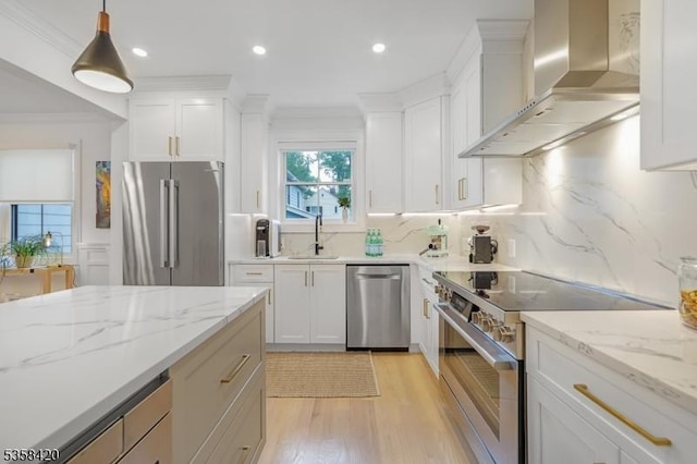 kitchen with high end appliances, wall chimney range hood, a sink, light wood-style floors, and white cabinets