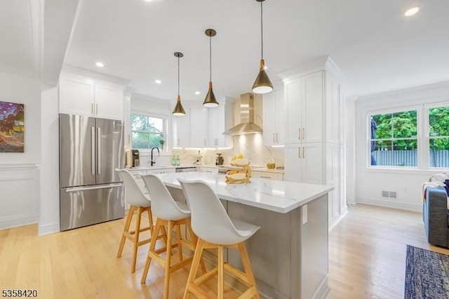 kitchen with freestanding refrigerator, wall chimney range hood, light wood-style floors, white cabinets, and a kitchen island