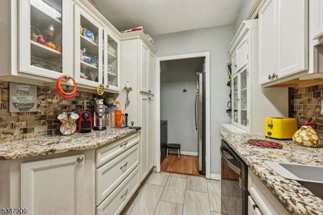 kitchen with dishwasher, backsplash, freestanding refrigerator, glass insert cabinets, and light stone counters