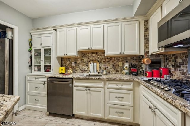 kitchen featuring appliances with stainless steel finishes, cream cabinetry, a sink, backsplash, and light stone counters