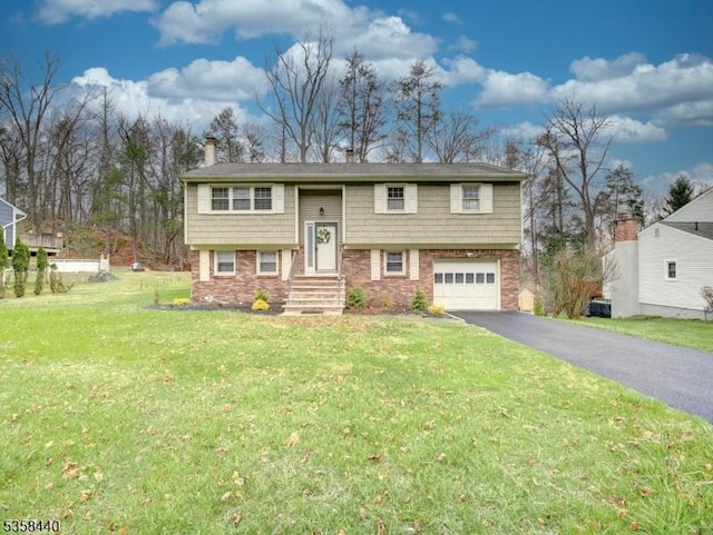 raised ranch with asphalt driveway, an attached garage, a front yard, a chimney, and brick siding
