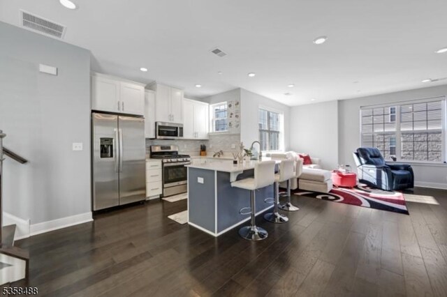 kitchen featuring stainless steel appliances, open floor plan, a kitchen bar, dark wood finished floors, and recessed lighting