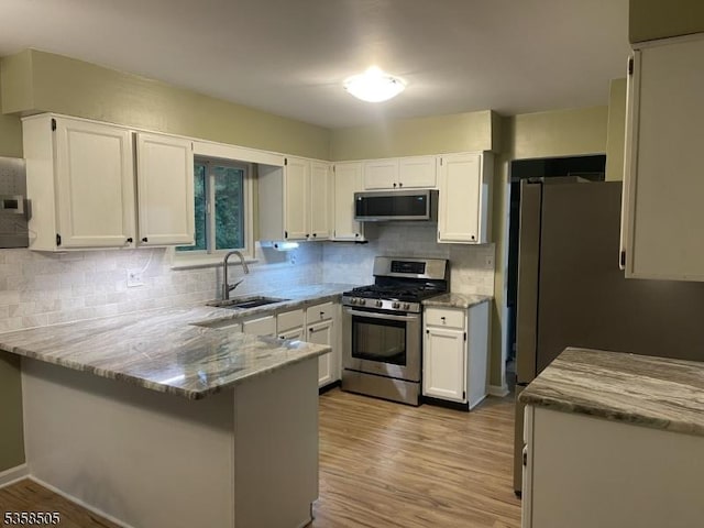 kitchen featuring stainless steel appliances, a sink, a peninsula, white cabinetry, and light wood-type flooring