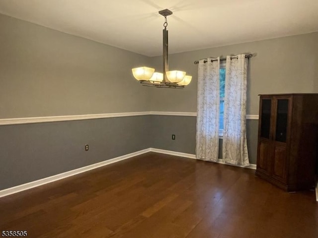 spare room featuring wood finished floors, a chandelier, and baseboards