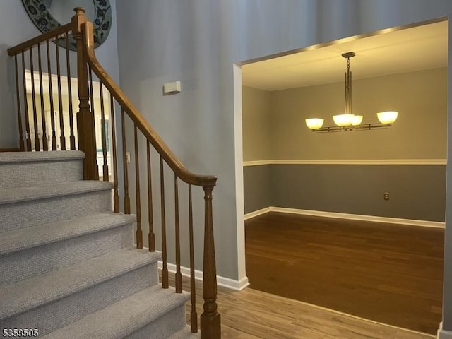 staircase with wood finished floors, a chandelier, and baseboards