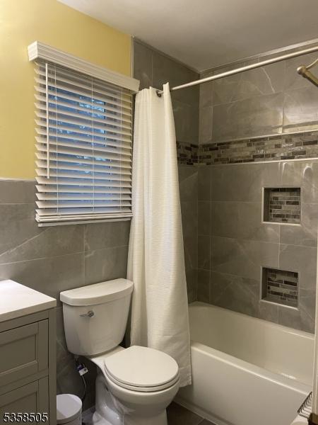 full bath with toilet, vanity, shower / bathtub combination with curtain, and tile walls