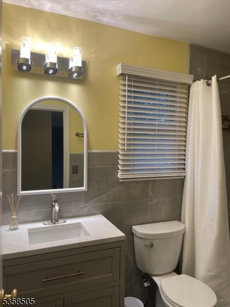 bathroom featuring tile walls, toilet, vanity, a shower with curtain, and a wainscoted wall