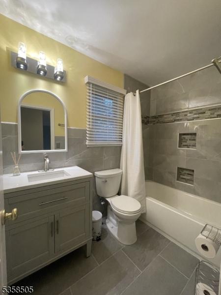 bathroom with tile walls, tile patterned floors, toilet, vanity, and shower / bath combination with curtain