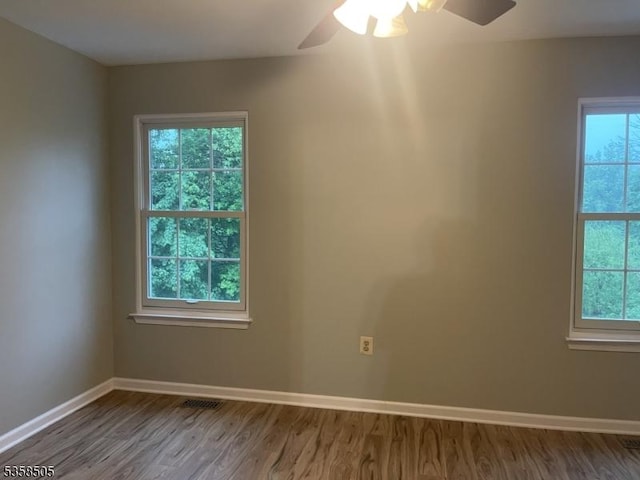 unfurnished room with healthy amount of natural light, wood finished floors, a ceiling fan, and baseboards