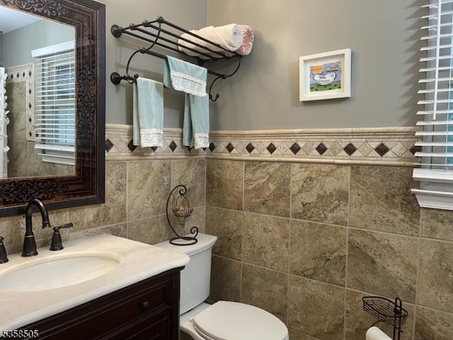 bathroom featuring tile walls, toilet, vanity, and wainscoting