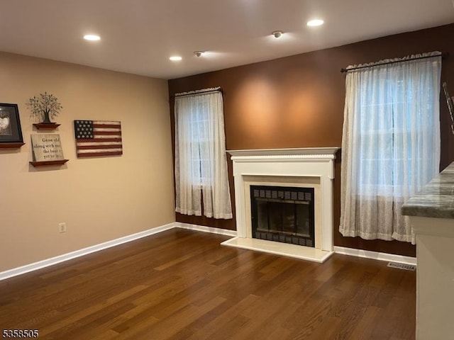 unfurnished living room with wood finished floors, baseboards, a fireplace with raised hearth, and recessed lighting