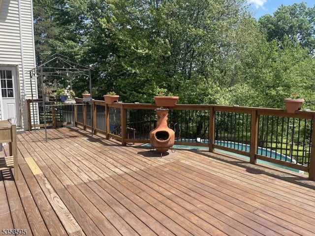 deck with a gazebo, a pool, and view of wooded area