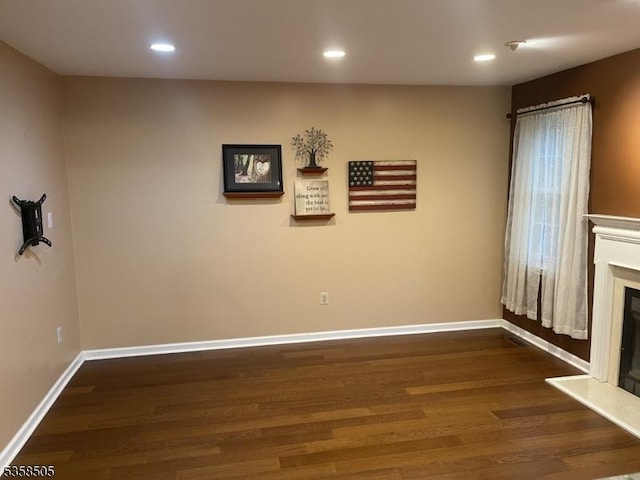 unfurnished living room featuring dark wood finished floors, baseboards, a fireplace with raised hearth, and recessed lighting