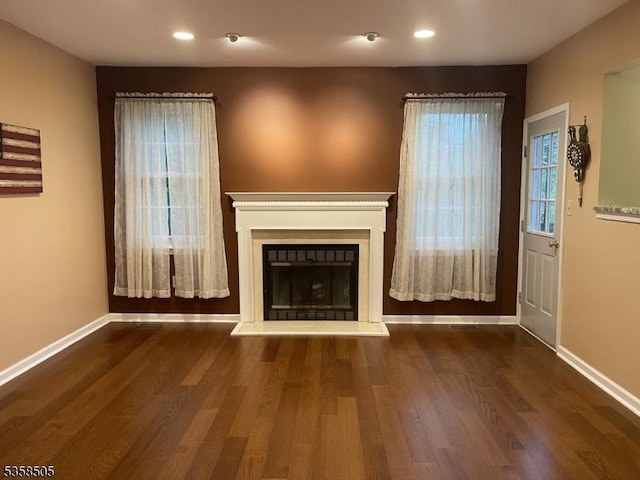 unfurnished living room with baseboards, recessed lighting, a fireplace with raised hearth, and wood finished floors
