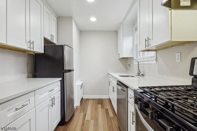 kitchen featuring appliances with stainless steel finishes, a sink, light wood-style flooring, white cabinets, and extractor fan