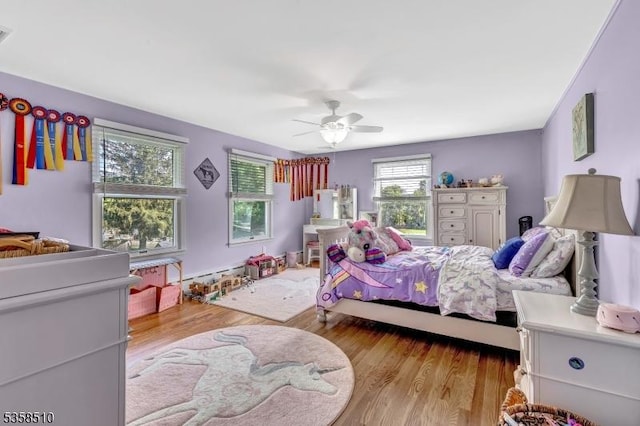 bedroom with wood finished floors, ceiling fan, and baseboard heating