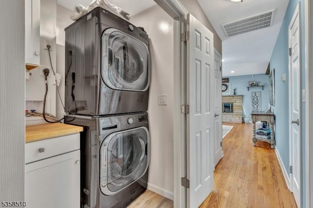 washroom featuring stacked washing machine and dryer, light wood finished floors, a fireplace, and baseboards