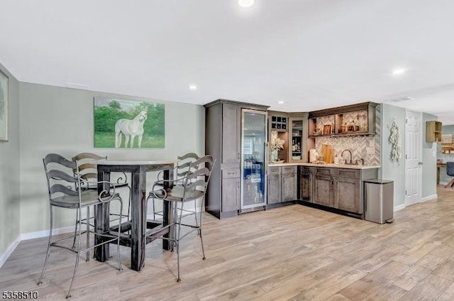 indoor wet bar with baseboards, tasteful backsplash, light wood-style flooring, and recessed lighting