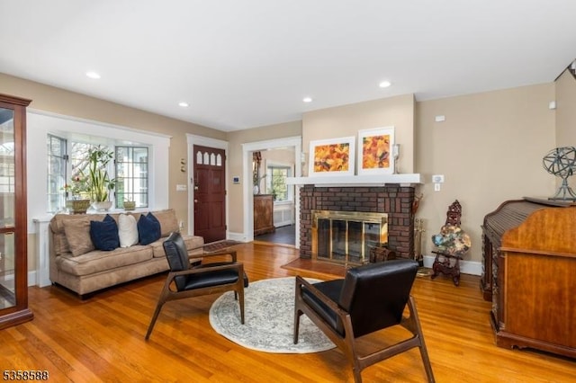 living room featuring light wood finished floors, baseboards, a brick fireplace, and recessed lighting