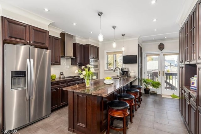 kitchen featuring appliances with stainless steel finishes, wall chimney range hood, a kitchen bar, backsplash, and dark stone countertops