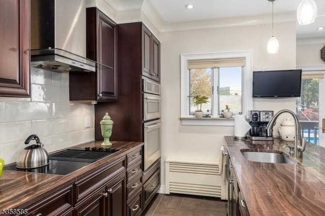 kitchen with wall chimney range hood, a sink, butcher block countertops, decorative backsplash, and pendant lighting