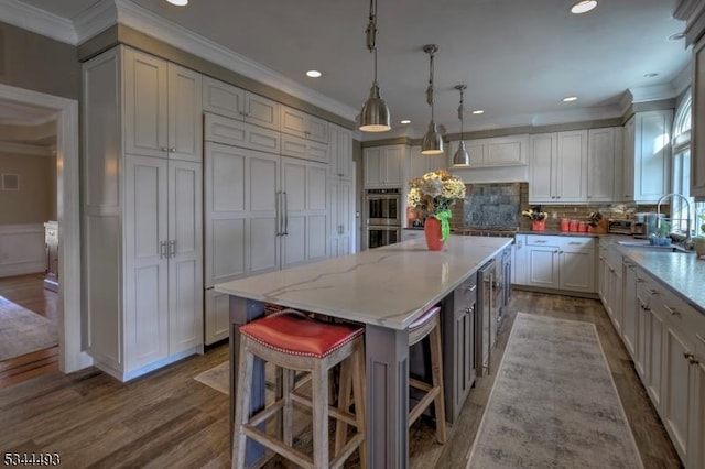 kitchen with stainless steel appliances, ornamental molding, a sink, a center island, and wood finished floors