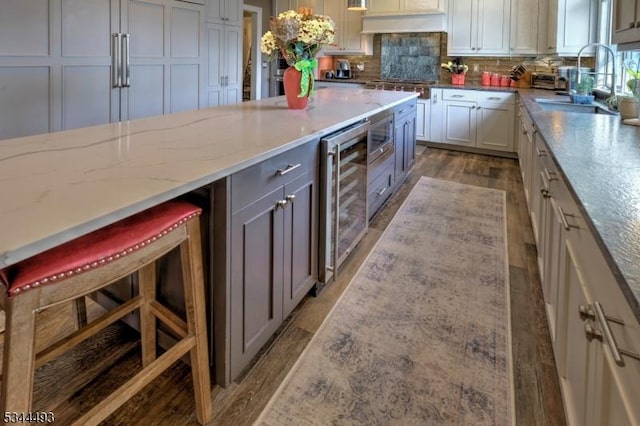 kitchen with a sink, wine cooler, wood finished floors, light stone counters, and backsplash