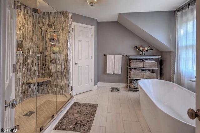 full bath featuring a shower stall, a freestanding bath, and baseboards