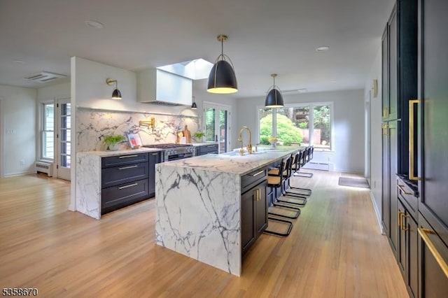 25 Highland Ave, Peapack Gladstone Boro, NJ 07931 - kitchen featuring a kitchen breakfast bar, light wood-style flooring, light stone countertops, an island with sink, and decorative backsplash