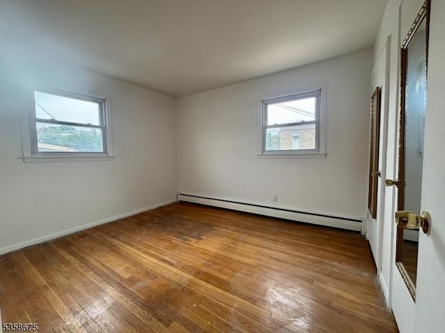 unfurnished room with baseboard heating, healthy amount of natural light, hardwood / wood-style flooring, and baseboards