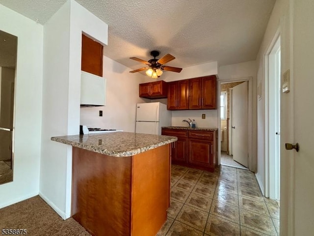 kitchen featuring freestanding refrigerator, a peninsula, a textured ceiling, ceiling fan, and a sink