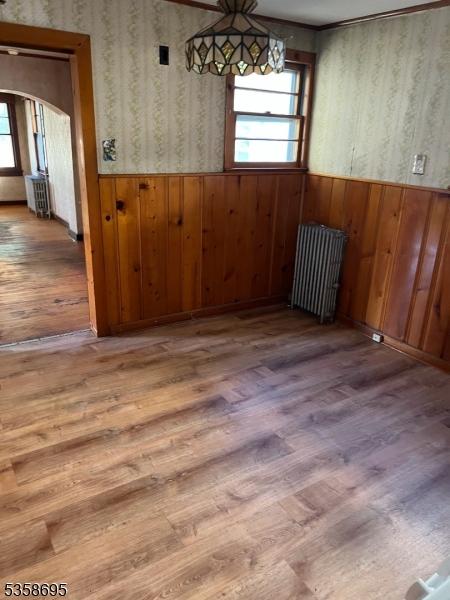 626 Tremont Ave, City Of Orange Twp, NJ 07050 - unfurnished dining area with wallpapered walls, radiator heating unit, a wainscoted wall, wood finished floors, and arched walkways