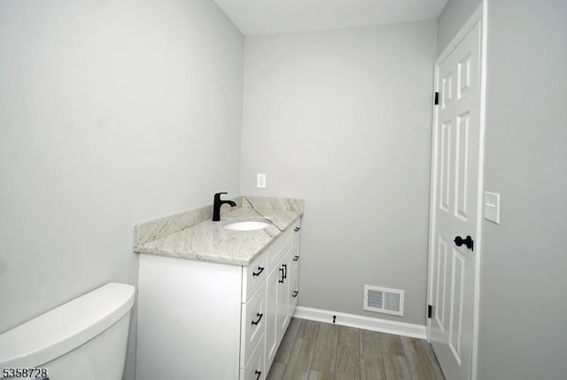 bathroom with vanity, toilet, wood finished floors, and baseboards