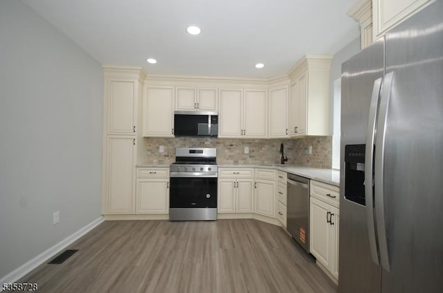 kitchen with appliances with stainless steel finishes, light countertops, light wood-style flooring, backsplash, and recessed lighting