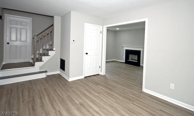 unfurnished living room featuring stairs, baseboards, wood finished floors, and a fireplace with flush hearth