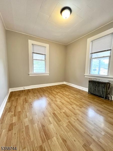 empty room with radiator, light wood finished floors, baseboards, and ornamental molding