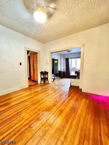 unfurnished room with light wood-style floors, a textured wall, and a textured ceiling