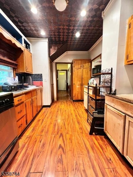 kitchen with an ornate ceiling, range, light wood finished floors, ornamental molding, and light countertops