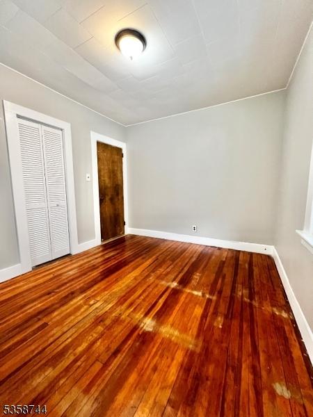unfurnished bedroom with hardwood / wood-style floors, baseboards, and a closet