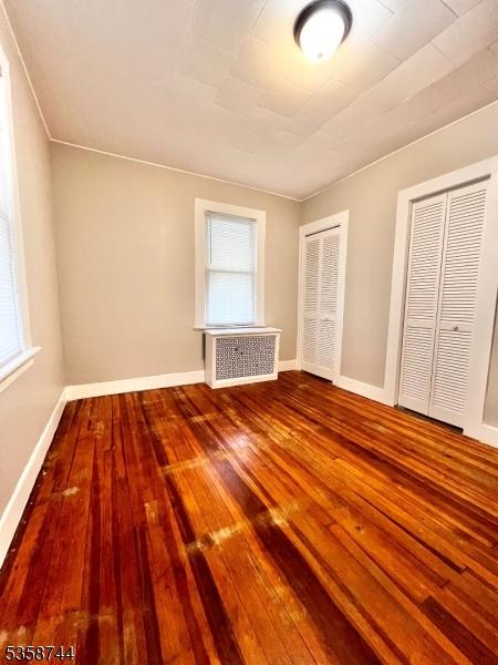 unfurnished bedroom with radiator heating unit, hardwood / wood-style flooring, multiple windows, and baseboards