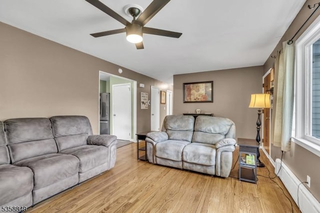 living room with a baseboard heating unit, ceiling fan, and light wood-style flooring