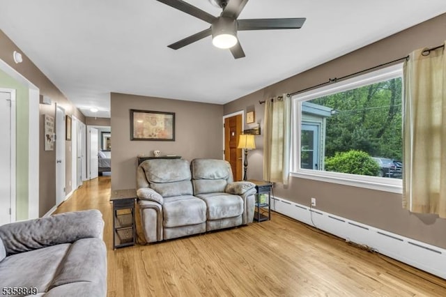 living room with baseboard heating, light wood finished floors, and ceiling fan
