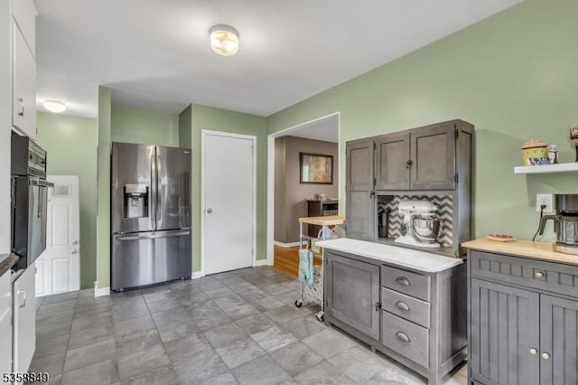 kitchen featuring stainless steel fridge, baseboards, light countertops, oven, and gray cabinetry