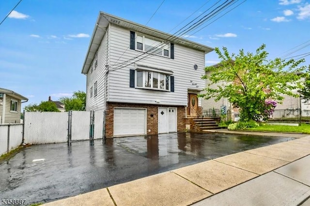 view of front of home with brick siding, an attached garage, driveway, and a gate