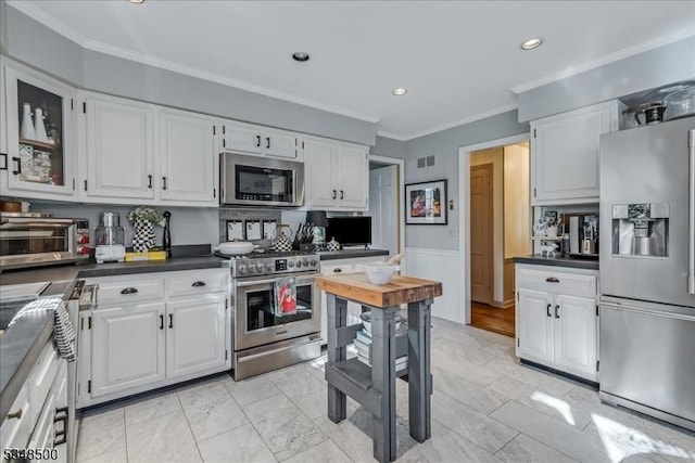 kitchen with stainless steel appliances, dark countertops, white cabinetry, ornamental molding, and recessed lighting