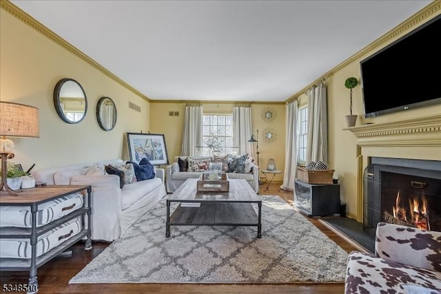 living room with dark wood finished floors, ornamental molding, and a warm lit fireplace
